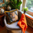 Load image into Gallery viewer, Chair with a tiger pillow and orange blanket in a room with plants and framed artwork.